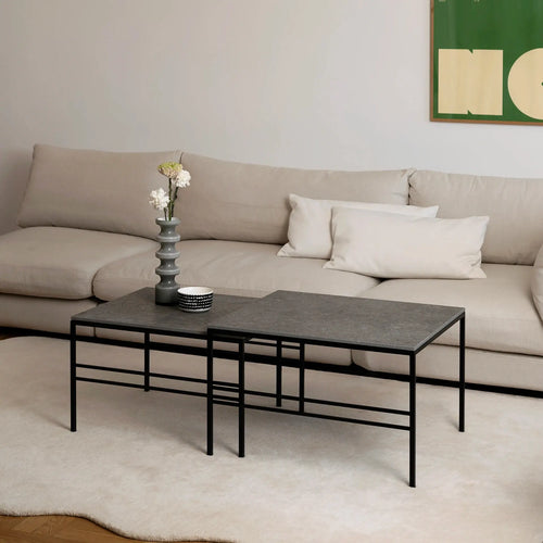 Minimalist Scandinavian living room featuring the Anton Coffee Table 2-set by by Crea in Grafite Dekton with a black steel frame. The nesting tables are styled with a sculptural grey vase and monochrome bowl, placed on a cream rug in front of a soft beige corner sofa.