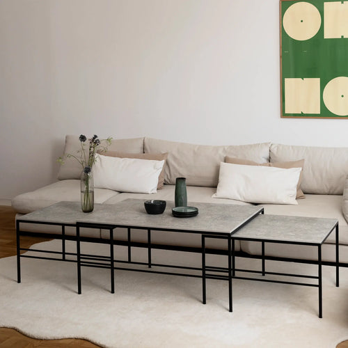 Modern living room featuring the Anton Coffee Table 3-set by by Crea in Grigio Dekton and black steel frame. The nesting tables are styled with ceramics and a glass vase, placed on a soft beige rug in front of a neutral Scandinavian sofa.