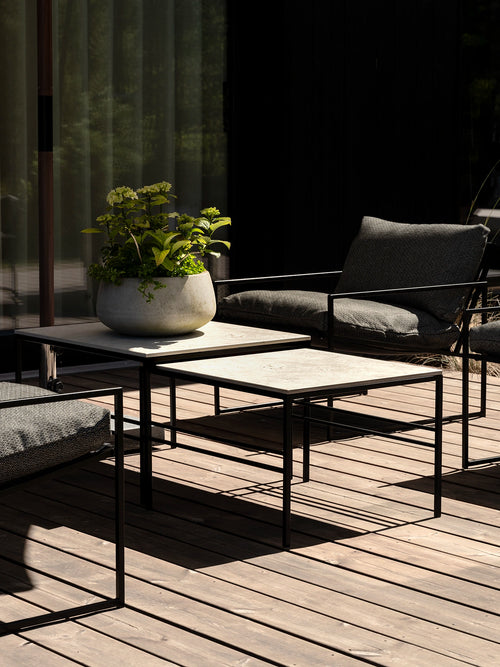 Anton outdoor lounge tables with light stone tops and black metal frames, paired with Kenny lounge chairs in textured Dusk cushions on a sunlit timber deck.