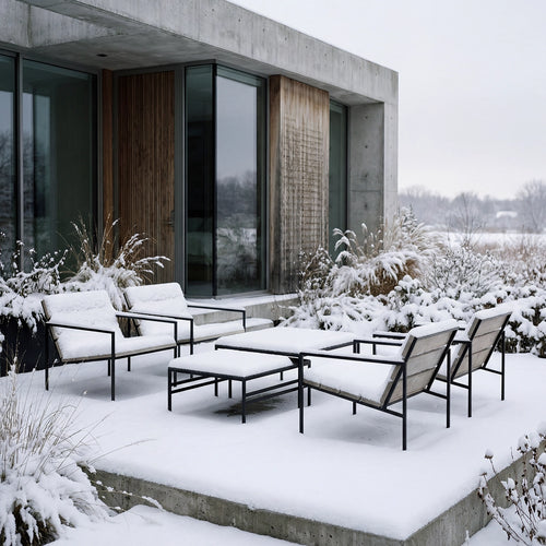 Outdoor lounge set with black steel frames and wooden details covered in snow, placed on a concrete terrace beside a modern Scandinavian home with glass walls and winter landscape.