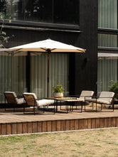The Arvid lounge group with four chairs in teak and black steel around slatted teak tables, gathered beneath a cream parasol on the deck.