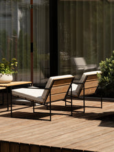 Two Arvid lounge chairs seen from behind, teak slat backs and slim black steel frames casting long shadows across the deck.
