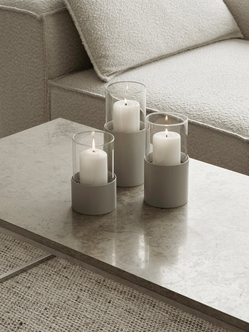 Three white candles in glass holders on a marble coffee table with a gray sofa in the background.
