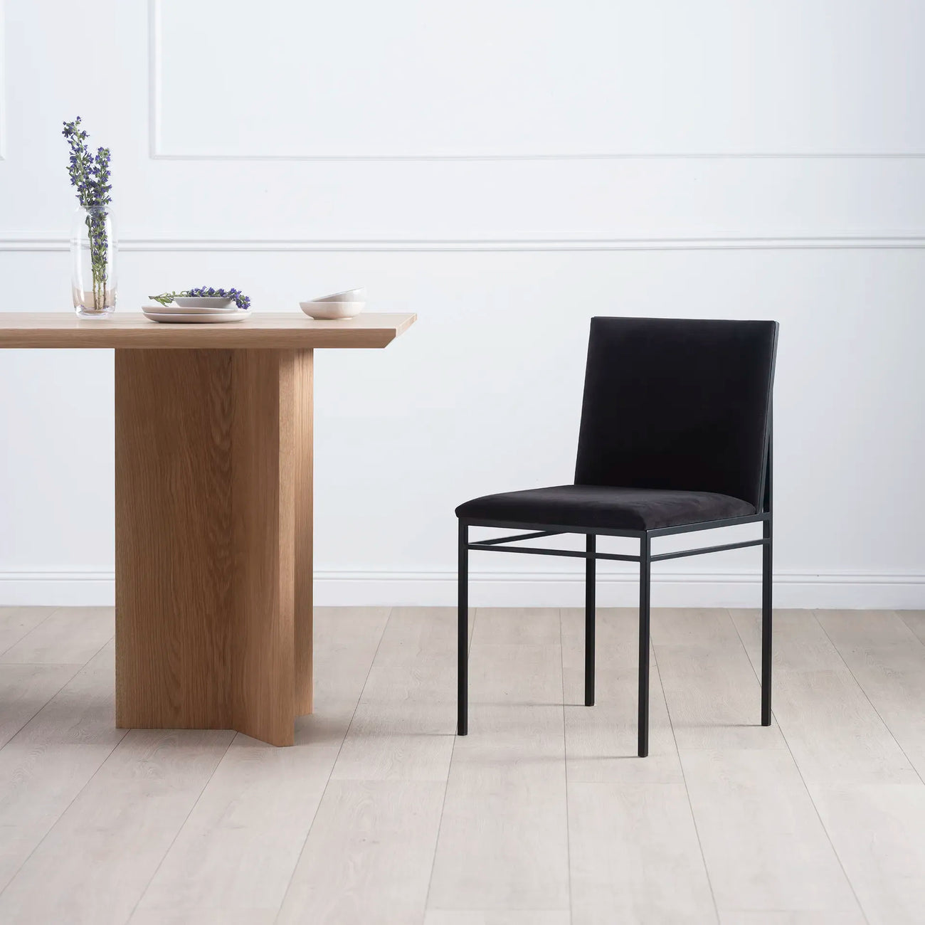 Bella dining chair in black velvet beside a wooden table, showcasing a minimalist design and sophisticated texture.