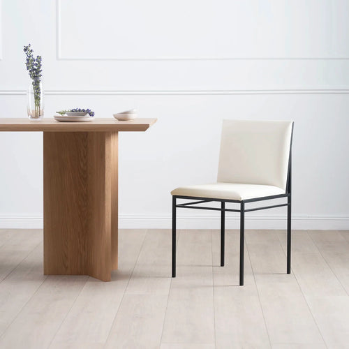 Bella dining chair in ivory leather with a modern black frame, beside a wooden dining table, enhancing minimalist decor.