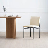 Dining chair Bella in sand leather with black frame beside a modern wooden dining table.
