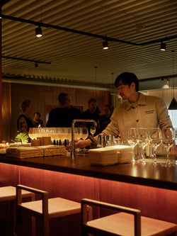 A bartender serving drinks behind the bar at Norrbottens Destilleri, with Ebba bar stools from by Crea in the foreground.