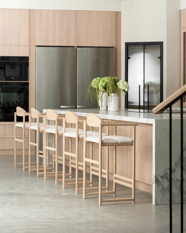 Carl bar stools in natural oak with ivory bouclé cushions, styled at a modern marble kitchen island in a Scandinavian-inspired home.