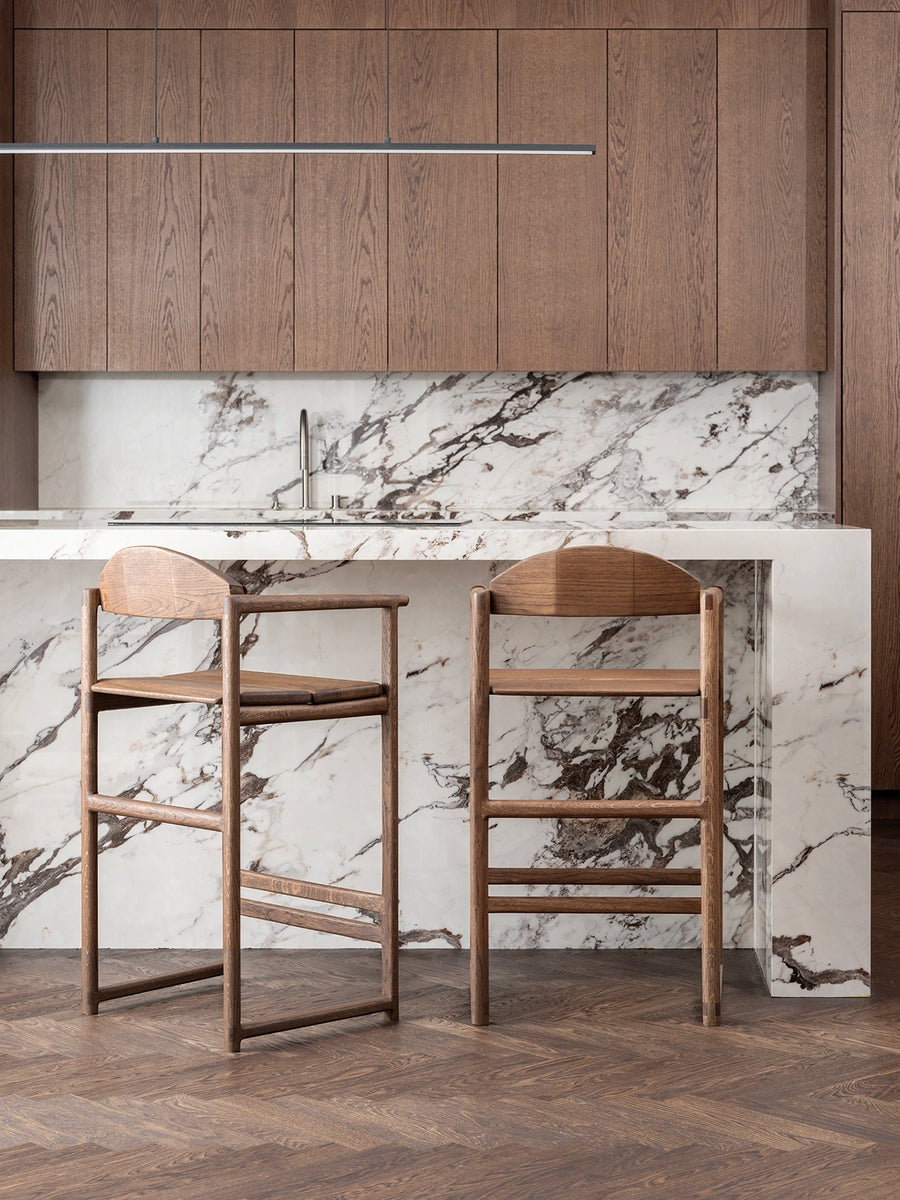Oak Bar Stool at a modern kitchen island with dark oak wood cabinets and marble countertop.