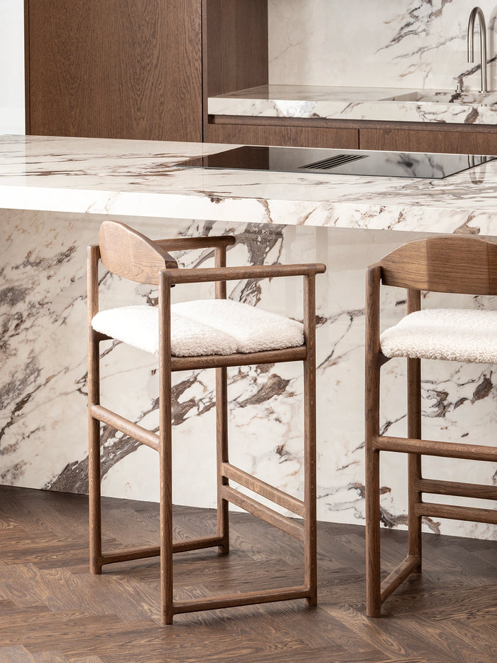 Oak Bar Stool Carl in dark oak with ivory bouclé in a modern kitchen setting with marble countertops.