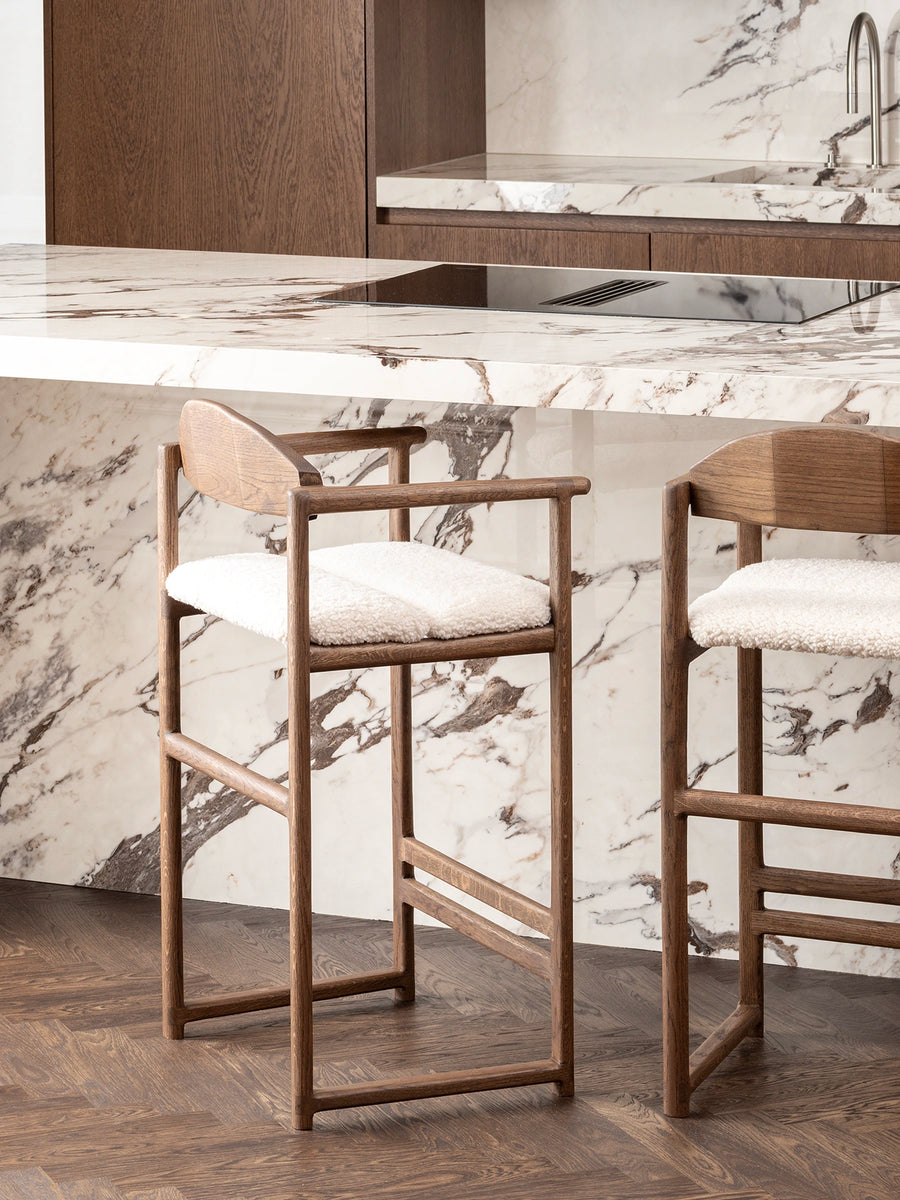 Oak Bar Stool Carl in dark oak with ivory bouclé in a modern kitchen setting with marble countertops.