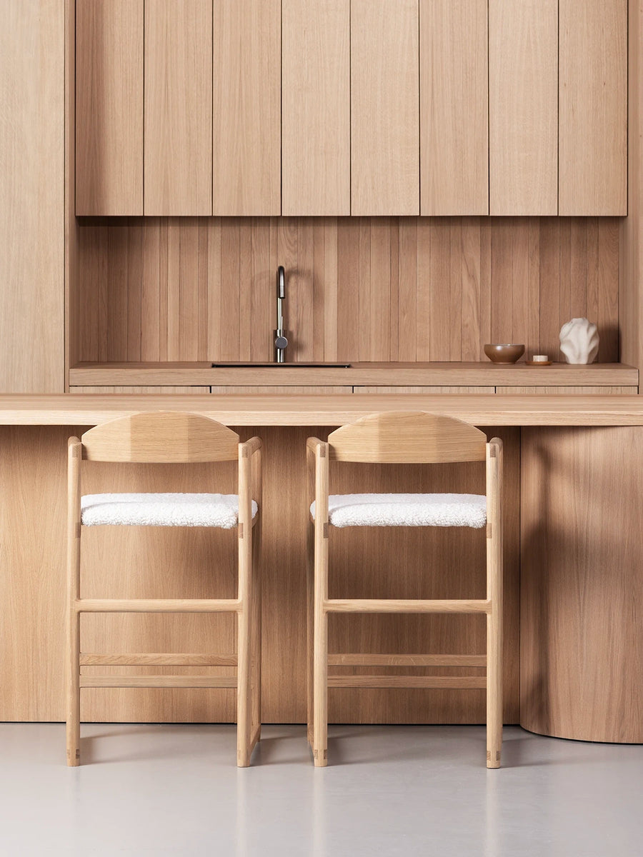 Minimalist Oak Bar Stool in a modern kitchen setting with warm wood accents and ivory bouclé seats.
