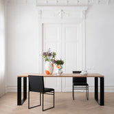 Front view of the Diana Dining Table featuring a solid oak top and black steel frame, styled with colorful ceramic vases and minimalist black dining chairs in an elegant Scandinavian interior.