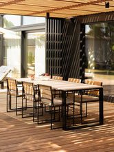 Diana outdoor dining table with a light Dekton top and black frame, paired with Signe teak dining chairs on a covered terrace.