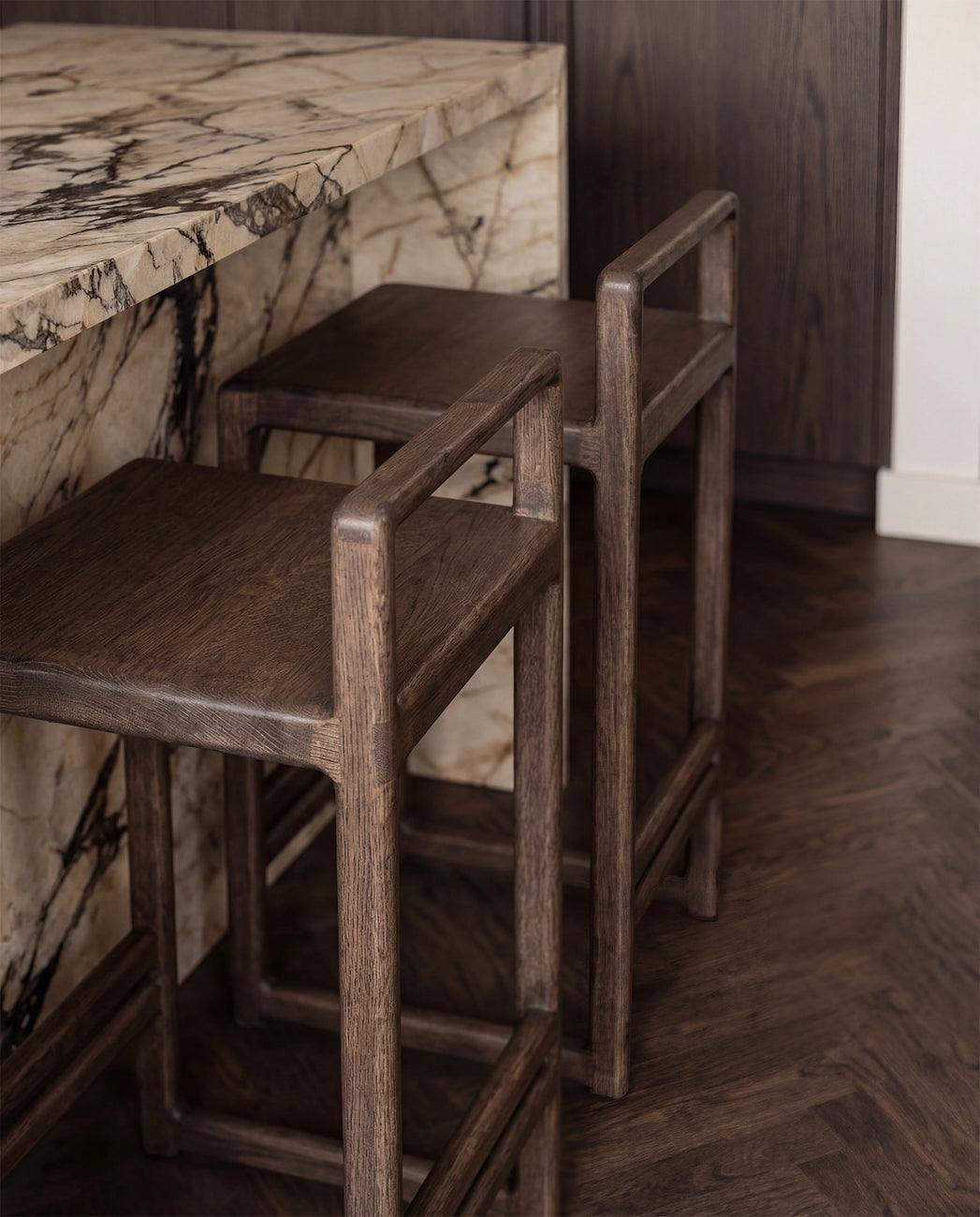 Close-up detail of Ebba bar stools in dark oak tucked under a marble kitchen island, highlighting the solid wood craftsmanship and natural grain texture in a refined Scandinavian interior.