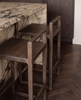 Close-up detail of Ebba bar stools in dark oak tucked under a marble kitchen island, highlighting the solid wood craftsmanship and natural grain texture in a refined Scandinavian interior.