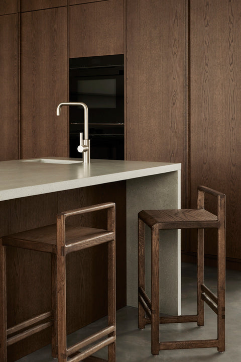 Ebba bar stools in dark-stained solid oak placed by a minimalist kitchen island in a Stockholm archipelago villa.