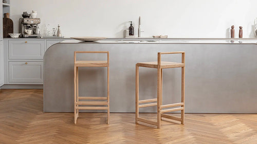 Ebba Bar Stools in natural oak placed at a curved concrete kitchen island, paired with herringbone parquet flooring and soft grey cabinetry in a Scandinavian-style kitchen.