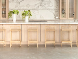 Ebba Bar Stools in natural oak lined up at a Scandinavian-style kitchen island, featuring a marble countertop and backsplash with light wood cabinetry and minimalist floral decor.