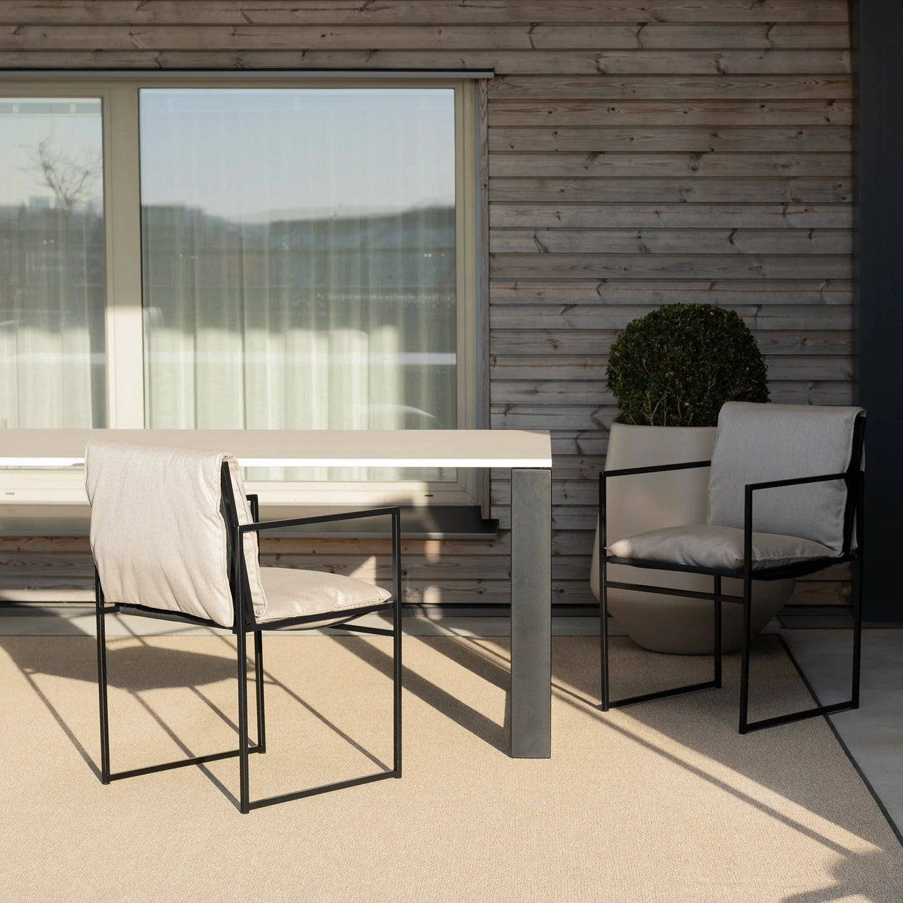 Elsy outdoor chair in black with fossil acrylic, positioned beside a sleek table in a modern outdoor setting.