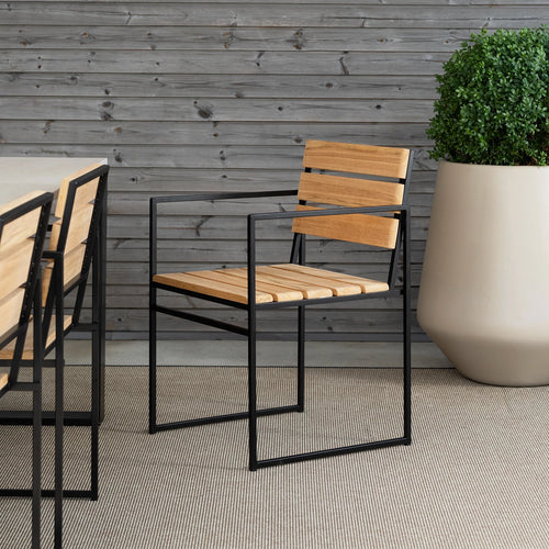 Elsy Outdoor Chair with armrests by by Crea, featuring teak wood and black steel frame. Handmade Scandinavian dining chair for modern patios, terraces, and sustainable outdoor furniture setups.