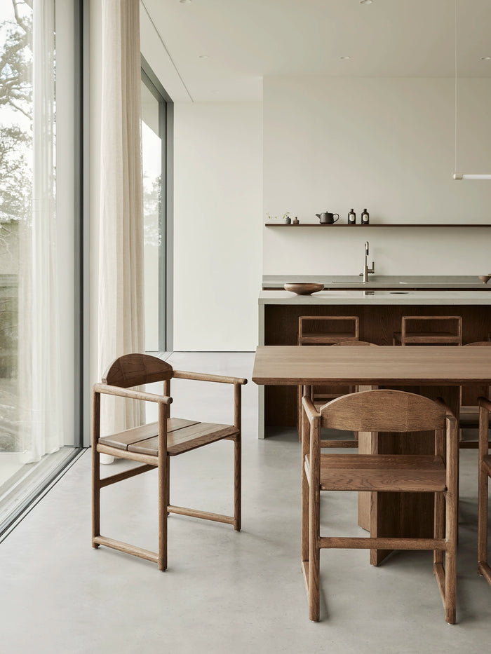 Erik dining chairs in solid dark oak styled in a minimalist Scandinavian kitchen interior with floor-to-ceiling windows, handcrafted oak furniture, and soft natural Nordic light.
