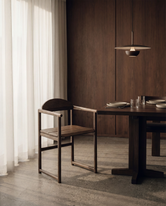 Erik dining chair in dark oak with armrests, solid wood Scandinavian design styled at a minimalist dining table with warm wood interior.