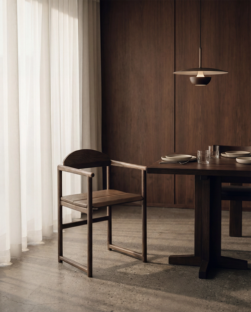 Erik dining chair in dark oak with armrests, solid wood Scandinavian design styled at a minimalist dining table with warm wood interior.