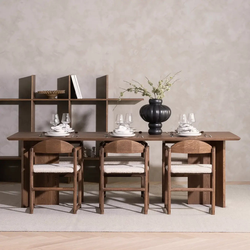 Dining chair Erik in dark oak frame with ivory bouclé cushion around modern dining table setting.