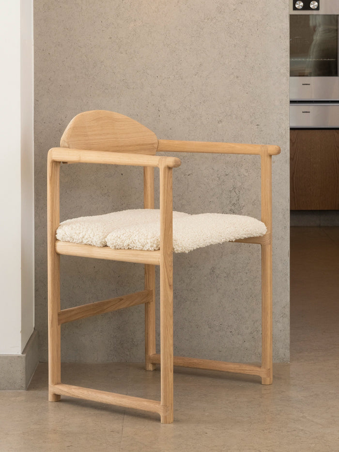Oak Dining Chair Erik in solid oak with an ivory bouclé cushion, shown alongside a dining setting
