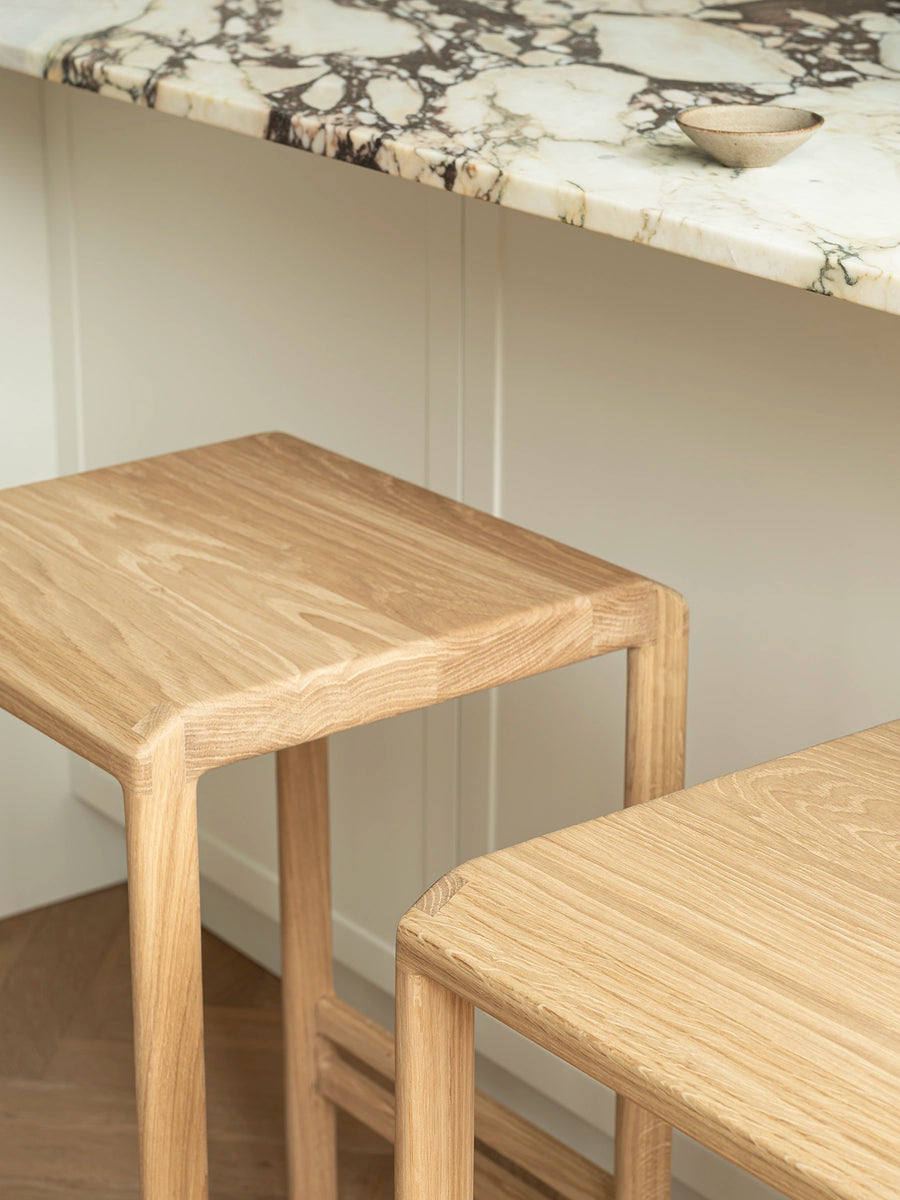 Solid oak bar stools styled beside a marble kitchen island in a refined Danish design kitchen with Scandinavian aesthetics.