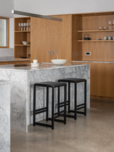 Modern kitchen with two black oak bar stools near a marble island countertop.
