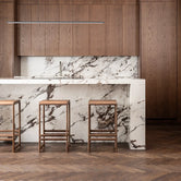 Oak Bar Stool Eva in dark oak at a modern kitchen counter with marble backsplash.