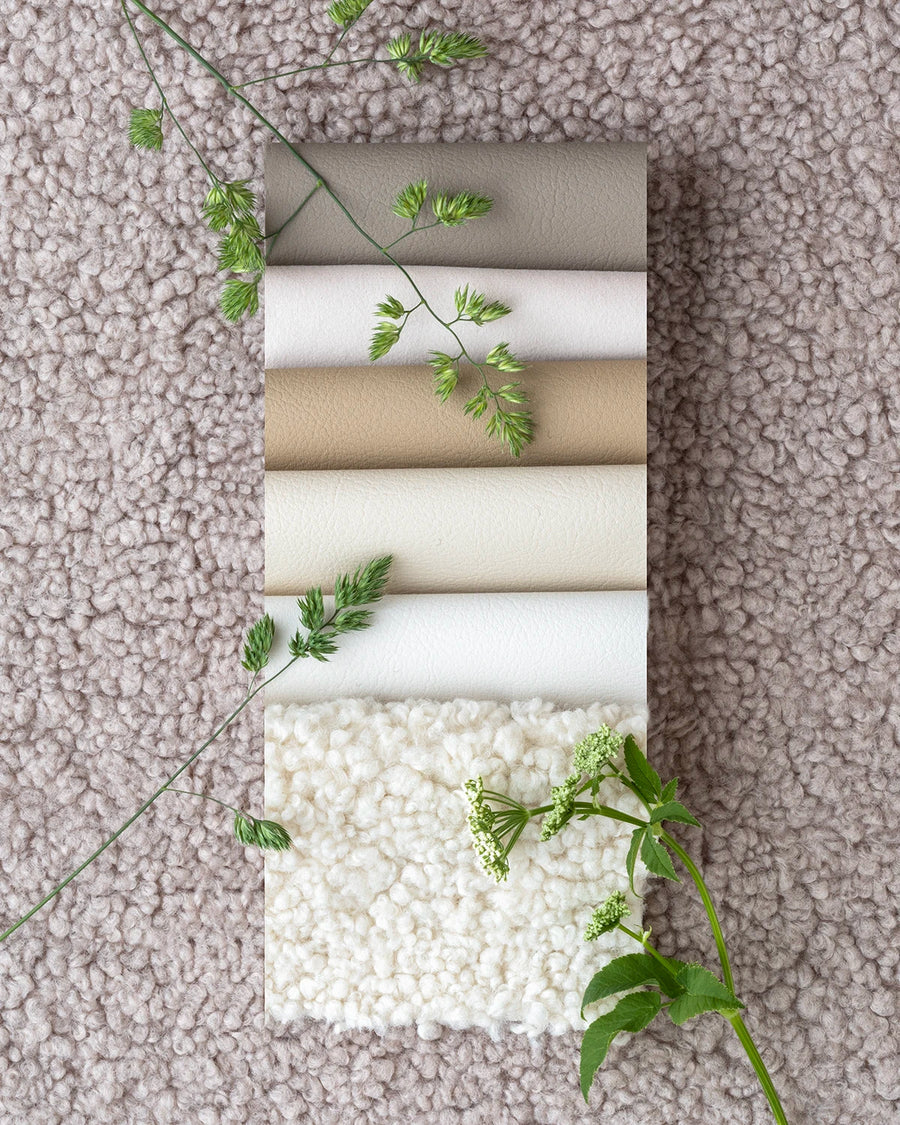 Collection of fabric samples in neutral tones with greenery on a textured surface, inviting tactile exploration.