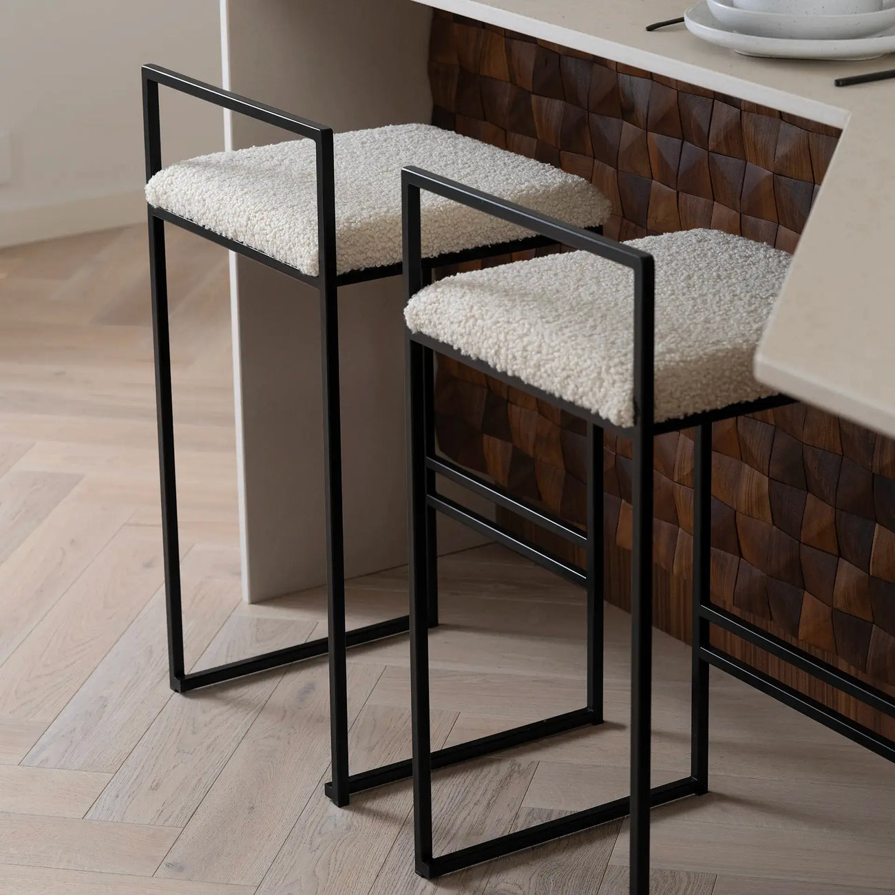 Freja bar stools with black frame and ivory bouclé cushions, stylish low backrest for comfort at the kitchen counter.