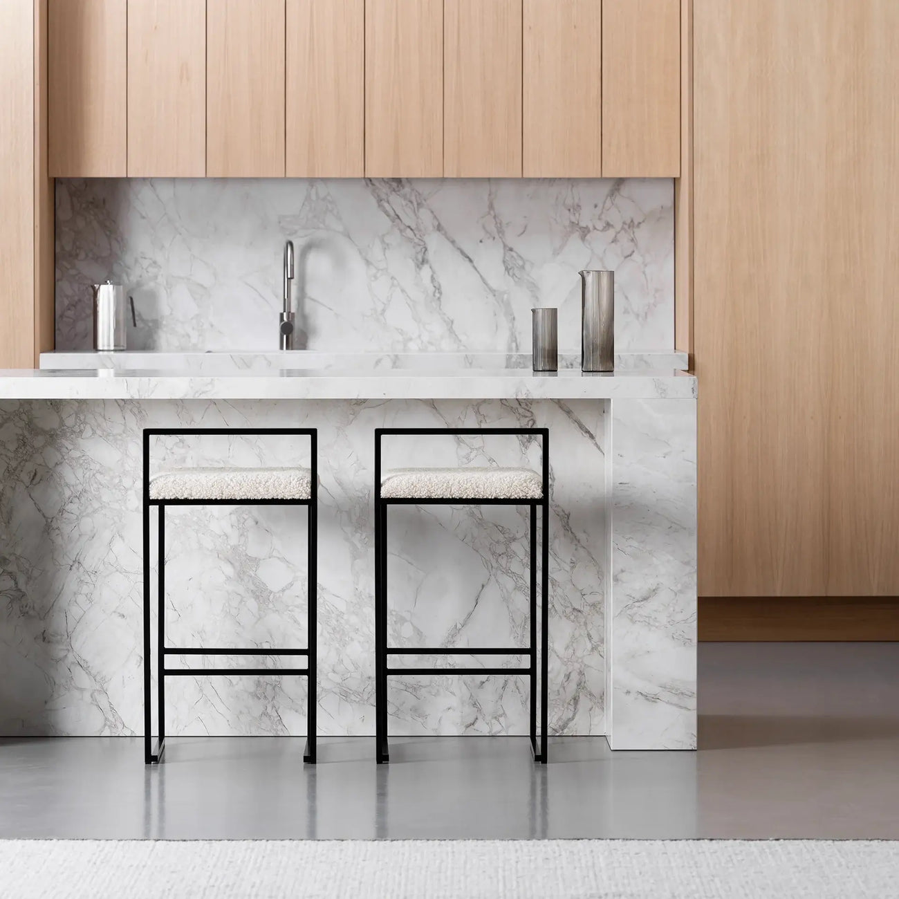 Freja bar stools with black frame and ivory bouclé cushions in modern kitchen with marble countertop.