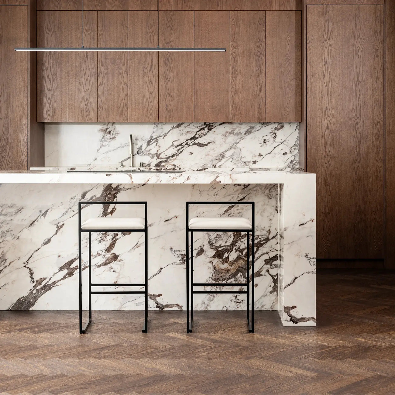 Freja bar stools with ivory leather cushions in modern kitchen with marble countertop and wooden cabinets.