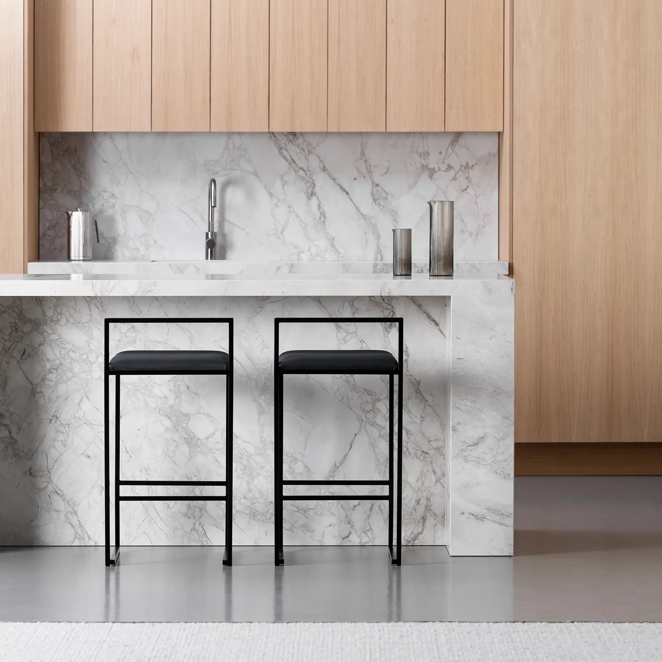 Freja bar stools in black leather with minimalist design at a modern kitchen island with marble countertop.