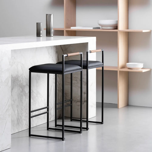 Freja bar stools in black leather with a sleek design, set against a modern kitchen backdrop with marble and wood.
