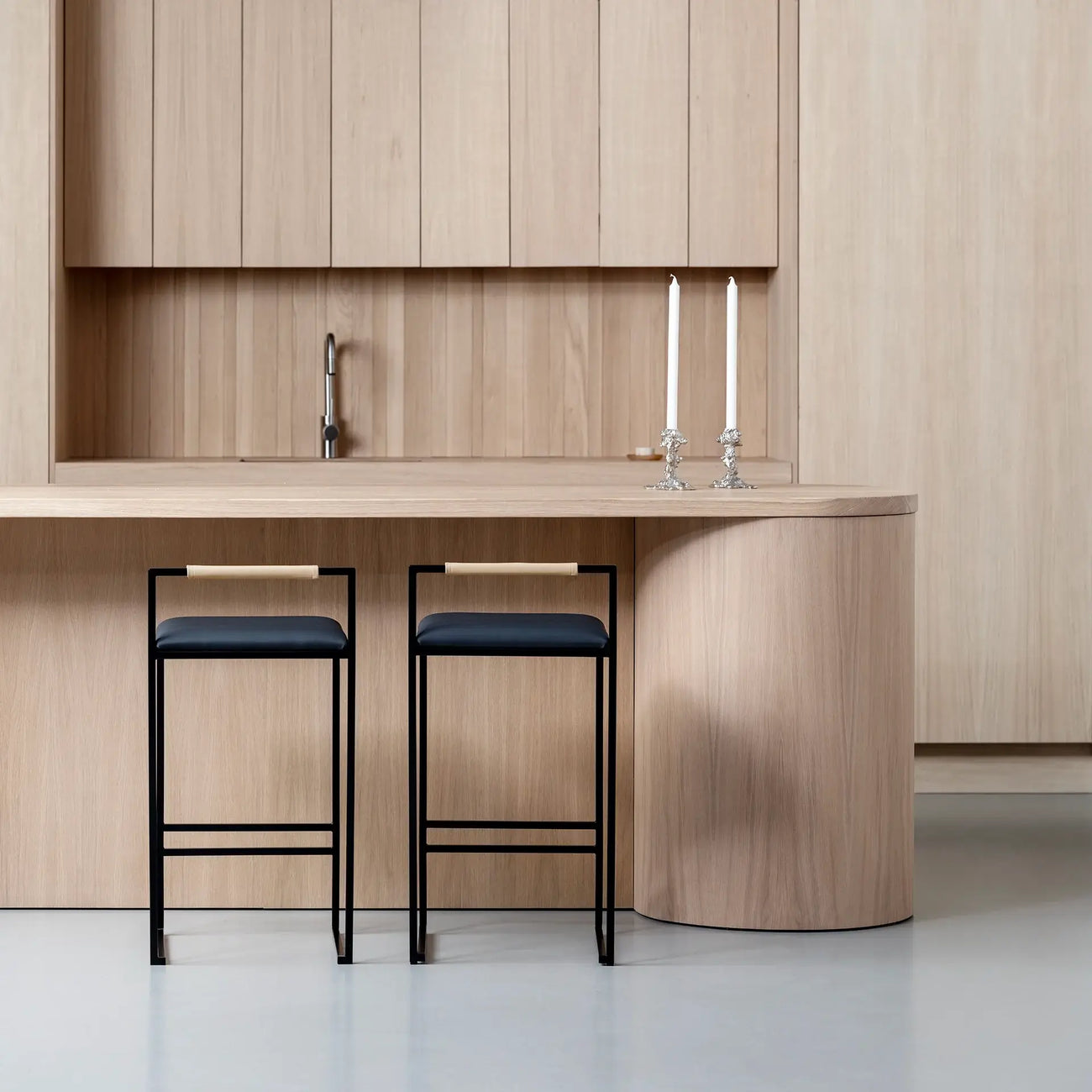 Freja bar stools with black leather seats and frame in a modern kitchen setting with wooden interiors.