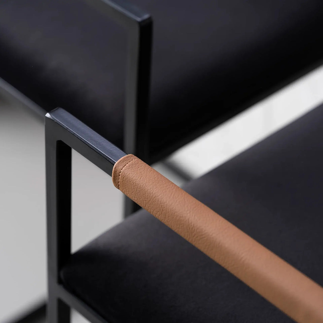Freja bar stool detail, featuring a black velvet seat and coffee bean leather armrest against a sleek black frame.