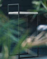 Outdoor Bar Stool Freja with black frame and fossil acrylic cushion against a dark background.