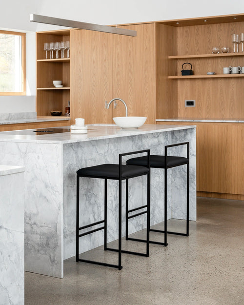 Modern kitchen with marble island, black stools, and wooden cabinets.