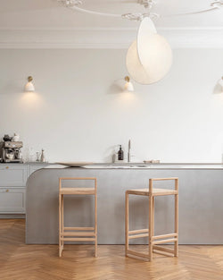 Two Ebba Bar Stools from by Crea in solid natural oak, styled at a soft grey minimalist kitchen island with herringbone oak flooring and Scandinavian interior detailing.