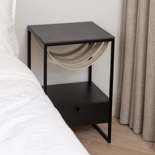 Sleek Iris bed table with black frame and Kelya dekton top, complementing bedroom decor beside a bed.