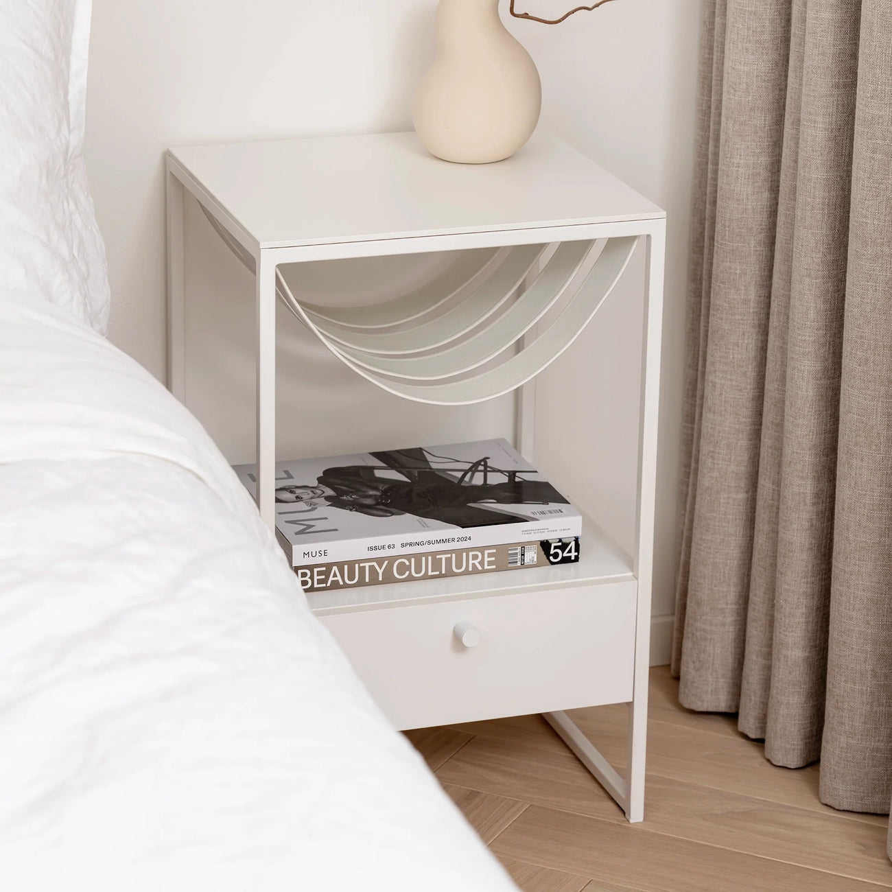 Iris bed table in white leather with sleek design, featuring a minimalistic tabletop and modern bedside storage.