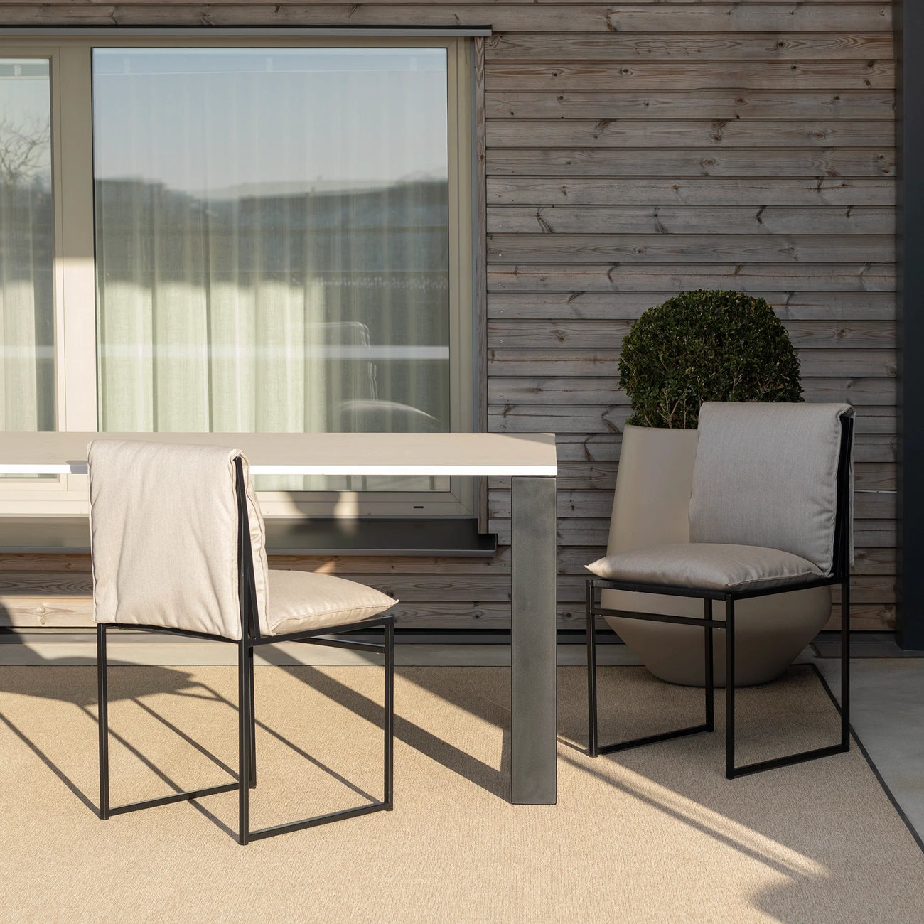 Minimalist Isa outdoor chairs in black frame with light cushions, paired with a stylish outdoor table on a patio.