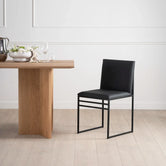 Isabell dining chair in black leather beside a wooden dining table in a minimalist setting, showcasing sleek design and comfort.