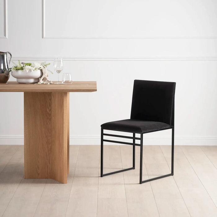Dining chair Isabell with black frame and jade black velvet cushion beside a wooden dining table.
