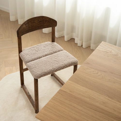 Karin dining chair in dark oak with greige bouclé seat, showcasing a warm, sculptural design in a modern dining space.